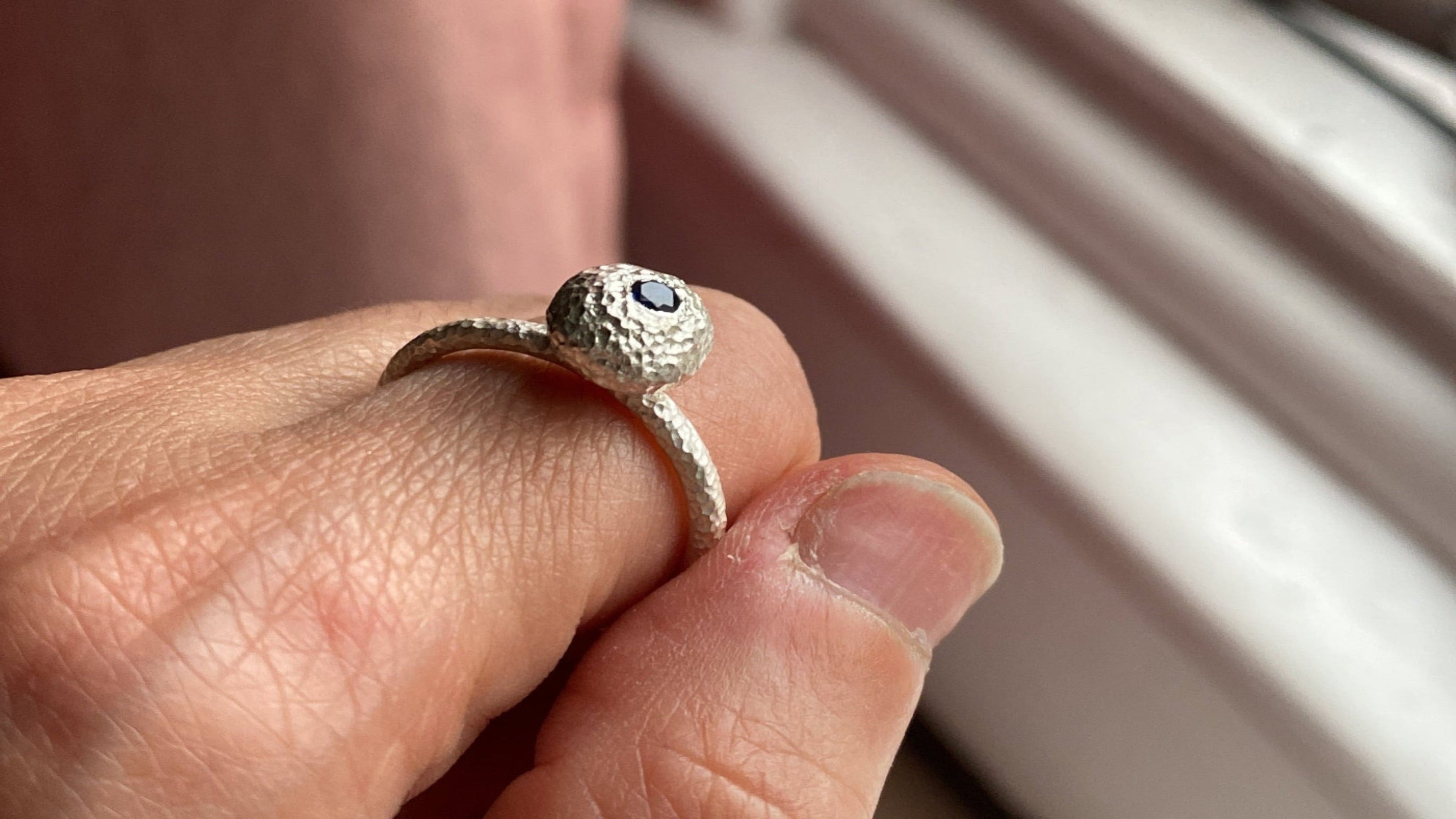 Silver ring with a blue stone on a finger against a neutral background